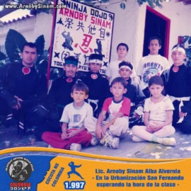 Fotografía histórica de alumnos y niños de la Urbanización San Fernando reunidos junto al Lic. Arnoby Sinam Alba antes del inicio de una clase del Ninja Dojo en 1997. Grupo de alumnos del Ninja Dojo Arnoby Sinam reunidos en la Urbanización San Fernando en 1997, esperando el inicio de una clase de Ninjutsu junto al letrero oficial de la academia.