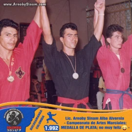 Arnoby Sinam Alba durante la ceremonia de premiación de un campeonato de artes marciales en 1992, obteniendo la medalla de plata en una destacada participación competitiva. Arnoby Sinam Alba recibiendo la medalla de plata durante un campeonato de artes marciales en 1992, junto a otros competidores en la ceremonia de premiación.