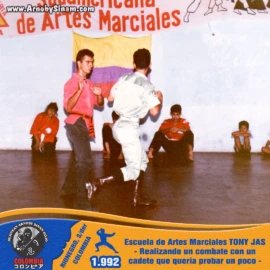 Arnoby Sinam participando en un combate de exhibición frente a estudiantes y asistentes de la Escuela de Artes Marciales Tony Jas, compartiendo conocimientos y experiencia marcial con un cadete invitado. Arnoby Sinam realizando un combate de exhibición contra un cadete durante una demostración de artes marciales en la Escuela Tony Jas en Bucaramanga en 1992.