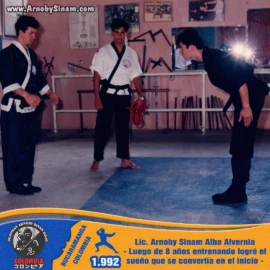 Momento de profundo respeto y gratitud luego de obtener el cinturón negro en 1992, un sueño alcanzado tras ocho años de constante entrenamiento y perseverancia. Arnoby Sinam realiza una reverencia de respeto tras recibir su cinturón negro en 1992, culminando ocho años de entrenamiento y dedicación a las artes marciales.